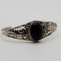 Beautiful black onyx Navajo cuff bracelet.  This piece features detailed sterling silver work featuring scrolls, flower and leaves crowned with a gorgeous black onyx gemstone. The amount of sterling silver work in this piece truly makes this handmade bracelet a real statement piece!   The diameter of this bracelet is 5.5" with a 1" gap.  It is 1" in width at the widest point. The one of a kind bracelet would make a wonderful gift for mom, birthday gift, gift for daughter, graduation gift, gift f Black Bohemian Bracelet Jewelry, Classic Adjustable Cuff Bracelet With Intricate Design, Black Oval Filigree Jewelry, Classic Black Filigree Jewelry, Oval Black Filigree Jewelry, Elegant Adjustable Engraved Jewelry, Elegant Handmade Black Bracelets, Elegant Black Handmade Bracelets, Elegant Black Jewelry With Intricate Design