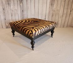 a zebra print footstool sitting on top of a white sheet covered floor next to a wooden wall