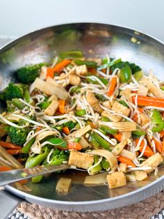 a stir fry with broccoli, carrots and noodles in a wok