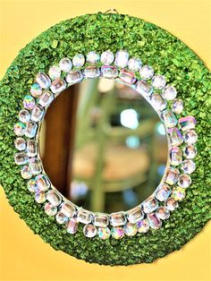 a mirror that is on the side of a wall covered in green grass and beads