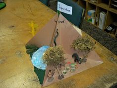 an origami pyramid made out of cardboard with trees and rocks in it on a table