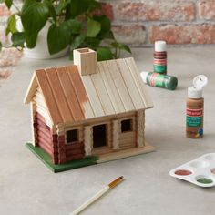 a wooden house sitting on top of a table next to paints and paintbrushes