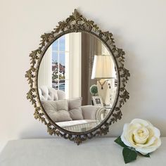 a mirror sitting on top of a table next to a white flower and a lamp