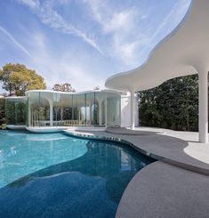 a large swimming pool in front of a white building with glass walls on the side