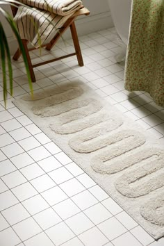 a bathroom with white tile flooring and rugs