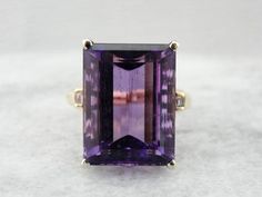 Dating to the 1960's, this solitaire cocktail ring was the height of fashion. One, simple, solitary gem, set up in the modernist style. Clean geometric lines were the order of the era. We've set this vintage mounting with a new Amethyst, in the finest of bright purple! Simple in shape, outstanding in color, this is a sophisticated statement piece, classic and classy at the same time. Metal: 14K Yellow and White Gold Stone: Fine Amethyst, 15 x 20 mm Emerald Cut, 22.08 Carats Accents Stone: 4 Bagu Modern Amethyst Ring With Accent Stones For Formal Events, Modern Amethyst Ring With Accent Stones For Formal Occasions, Elegant Rectangular Amethyst Ring For Formal Occasions, Modern Emerald Cut Amethyst Ring, Modern Amethyst Ring With Center Stone For Formal Occasions, Amethyst Cocktail Ring, Rectangle Ring, Amethyst Gem, Bright Purple