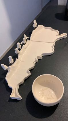 a white bowl sitting on top of a counter next to a ceramic sculpture with birds perched on it