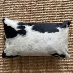 a black and white cowhide pillow sitting on a brown carpeted area with a tan wall behind it