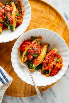 two white bowls filled with pasta and sauce on top of a wooden tray next to a fork