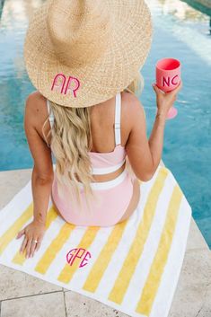 a woman sitting on top of a towel next to a pool holding a pink cup