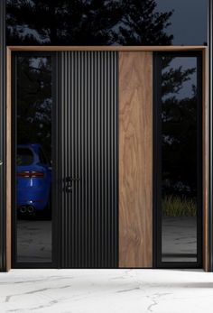 a blue car is parked in front of a wooden door with glass panels on it