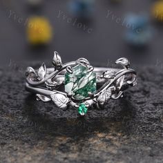 a close up view of a ring with leaves and green stone in the center on a rock