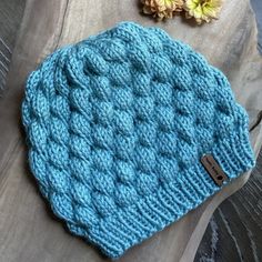 a blue knitted hat sitting on top of a wooden table next to a flower