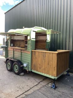 an old green trailer is parked in front of a building with a awning on it