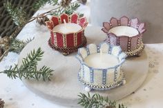 three candles sitting on top of a white plate next to pine cones and evergreen branches