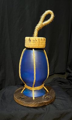 a blue vase with a rope wrapped around it on top of a wooden stand in front of a black backdrop