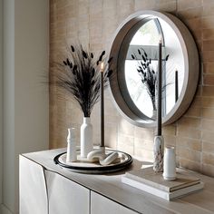 a table with some vases and candles on it next to a round wall mirror