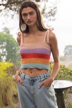 a woman wearing jeans and a crop top standing in front of a tree with her hands on her hips