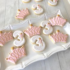 decorated cookies with pink and white frosting on a tray next to other cookies in the shape of crowns