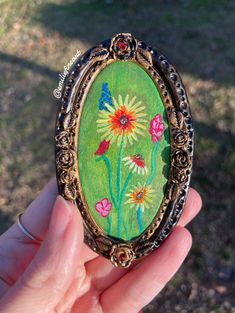 a person holding up a small painting in front of their face with flowers painted on it