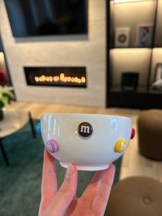 a person holding up a white bowl with stickers on it in front of a fireplace