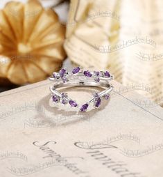 a ring with amethyst purple stones sits on top of a book next to some flowers