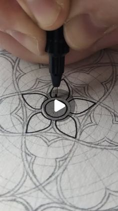 someone is drawing on paper with a pen and inking the design in front of them