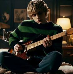 a young man sitting on top of a bed holding a guitar in front of him