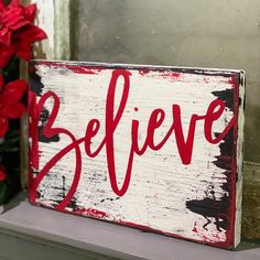 a red and white sign that says believe next to some poinsettis on a window sill