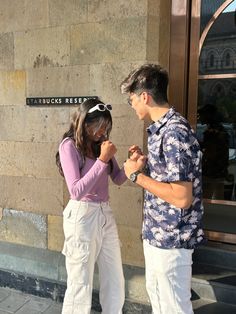 a young man and woman standing next to each other in front of a building holding hands