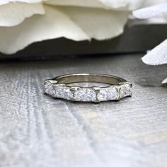 a wedding band with five diamonds on it sitting next to a white carnation flower