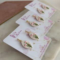 three pairs of earrings with pink flowers on them sitting on top of a piece of paper