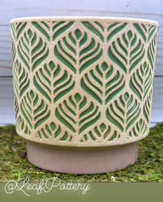 a green planter sitting on top of a moss covered ground next to a white wall