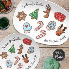 two plates with christmas cookies on them next to some candies and cupcakes