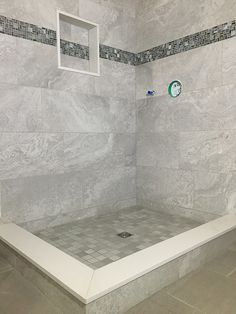 a tiled shower stall in a bathroom with white tile walls and floor tiles on the wall