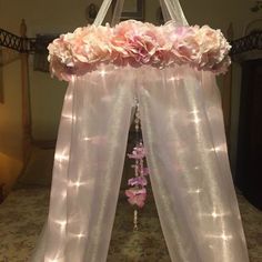 a canopy with pink flowers and lights hanging from it's sides in front of a bed