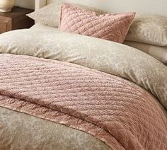 a bed with pink and beige comforters in a bedroom next to a night stand