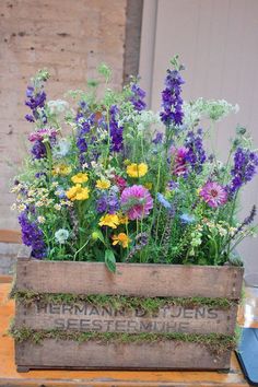 a wooden box filled with lots of different types of flowers on top of a table