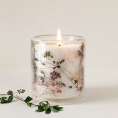 a glass candle with flowers on it next to some leaves and twigs in front of a white background