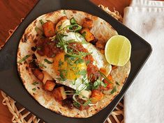 a tortilla topped with an egg, meat and veggies on a black plate