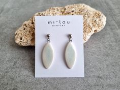 a pair of white earrings sitting on top of a piece of paper next to a rock