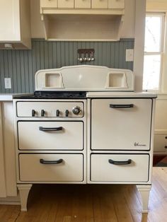 an old fashioned stove in a kitchen with white cabinets and wood flooring on the side