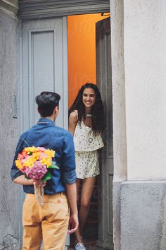 a man standing next to a woman in front of an open door with flowers on it