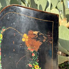 an old wooden box with flowers painted on it's front and back sides, sitting next to a cactus plant