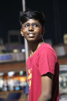 a young man wearing glasses standing in front of a building at night with his hands on his hips