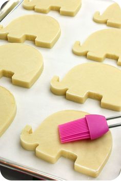 a pink brush sitting on top of a pan filled with cut out elephant shaped cookies