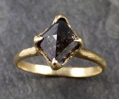 a gold ring with a black diamond in it on a gray stone surface, close up