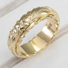 a gold wedding ring with an intricate design on the outside and inside, sitting on a white surface