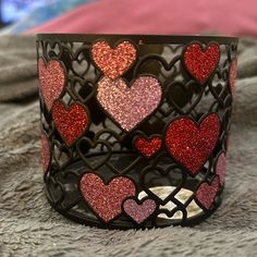 a decorative candle holder with hearts painted on the side and inside, sitting on a bed