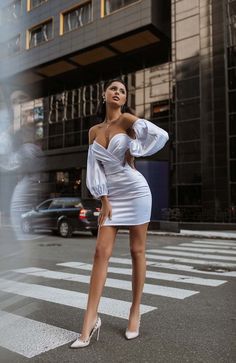 a woman in a white dress is standing on the street